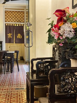 A traditional room with a patterned floor, wooden furniture, and a decorative vase with flowers. - Nam Keng Hotel (George Town)