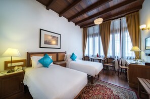 A hotel room with two beds, a desk, a chair, a small table, and a window with curtains. - Nam Keng Hotel (George Town)