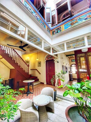 A multi-level atrium with a staircase, a dining area with wicker furniture, and a red door. - Nam Keng Hotel (George Town)