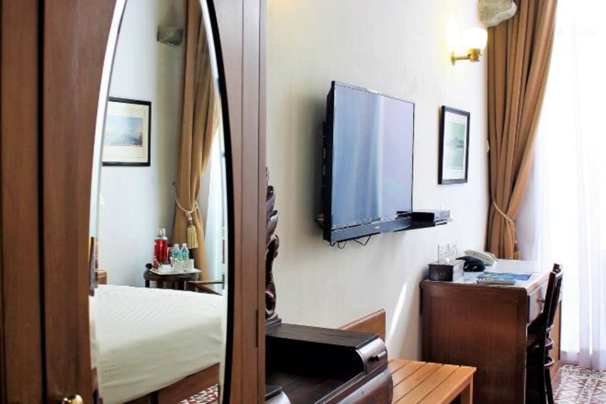 A hotel room with a bed, a desk with a chair, a television mounted on the wall, and a window with curtains.