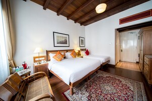 Une chambre d’hôtel avec deux lits, des meubles en bois, un tapis rouge à motifs et un plafond en bois.