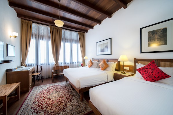 Habitación de hotel con dos camas, un escritorio, una silla, una lámpara de escritorio y un gran ventanal con cortinas.