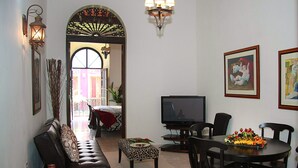 A living room with a sofa, a television, a dining table with chairs, and a decorative archway. - Fortaleza Suites (San Juan)