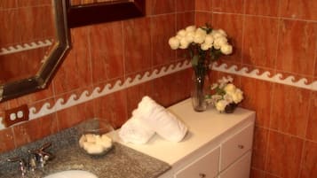 Un baño con encimera de granito, lavabo blanco y espejo. Hay toallas y un florero con flores sobre la encimera.