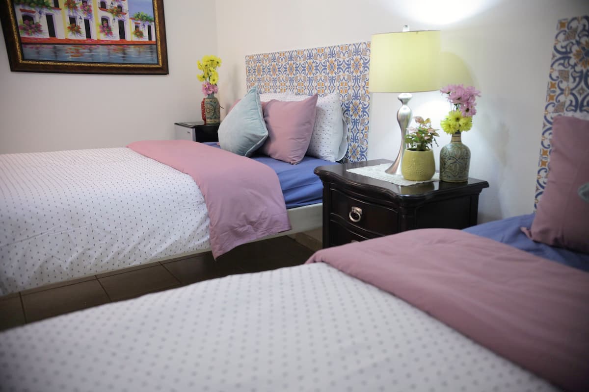 A bedroom with two beds, a nightstand, a lamp, and a wall-mounted painting.