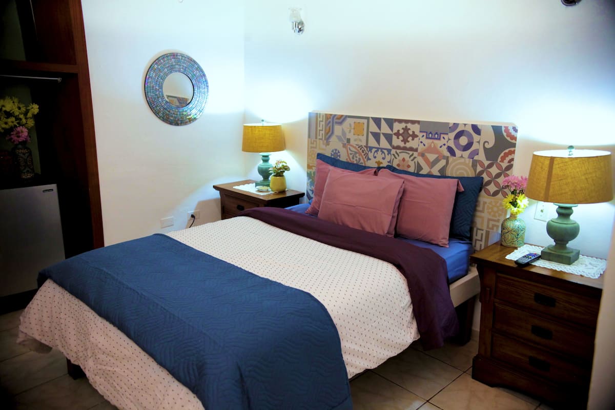 A bedroom with a bed, two bedside tables with lamps, a mirror, and a decorative headboard.