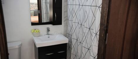 A bathroom with a white sink, black cabinets, a mirror, and a patterned shower curtain.