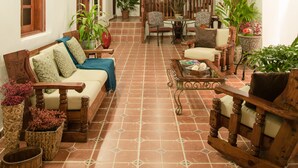 A cozy living room with a wooden ceiling, a sofa, chairs, and potted plants. - Fortaleza Suites (San Juan)