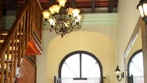 A cozy interior with a wooden staircase, a chandelier, two patterned armchairs, and a dining table with a vase of flowers. - Fortaleza Suites (San Juan)