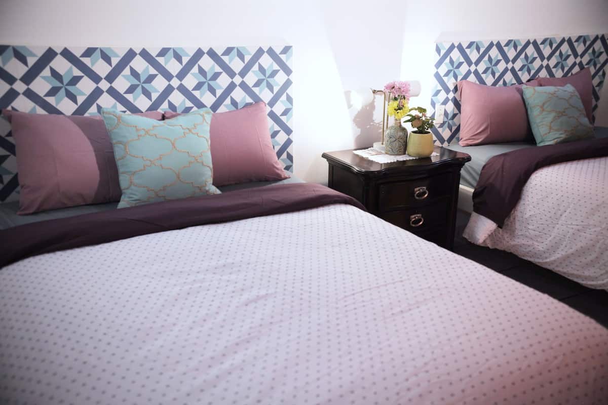 A bedroom with two beds, each with a patterned headboard, a nightstand with a vase of flowers, and a dresser with drawers.