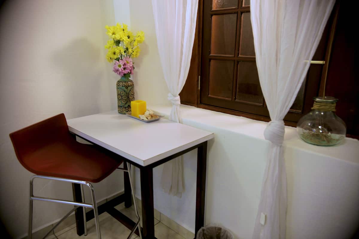 A small dining area with a table, a chair, a vase with flowers, a candle, and a window with curtains.