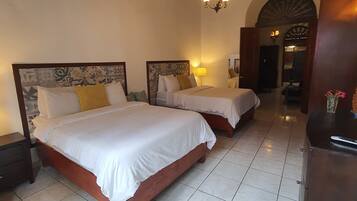 A hotel room with two beds, a wooden ceiling, tiled flooring, and a small desk.