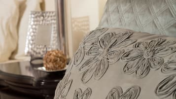Una cama con un cojín estampado, una lámpara de noche y un espejo decorativo sobre una mesita de noche.
