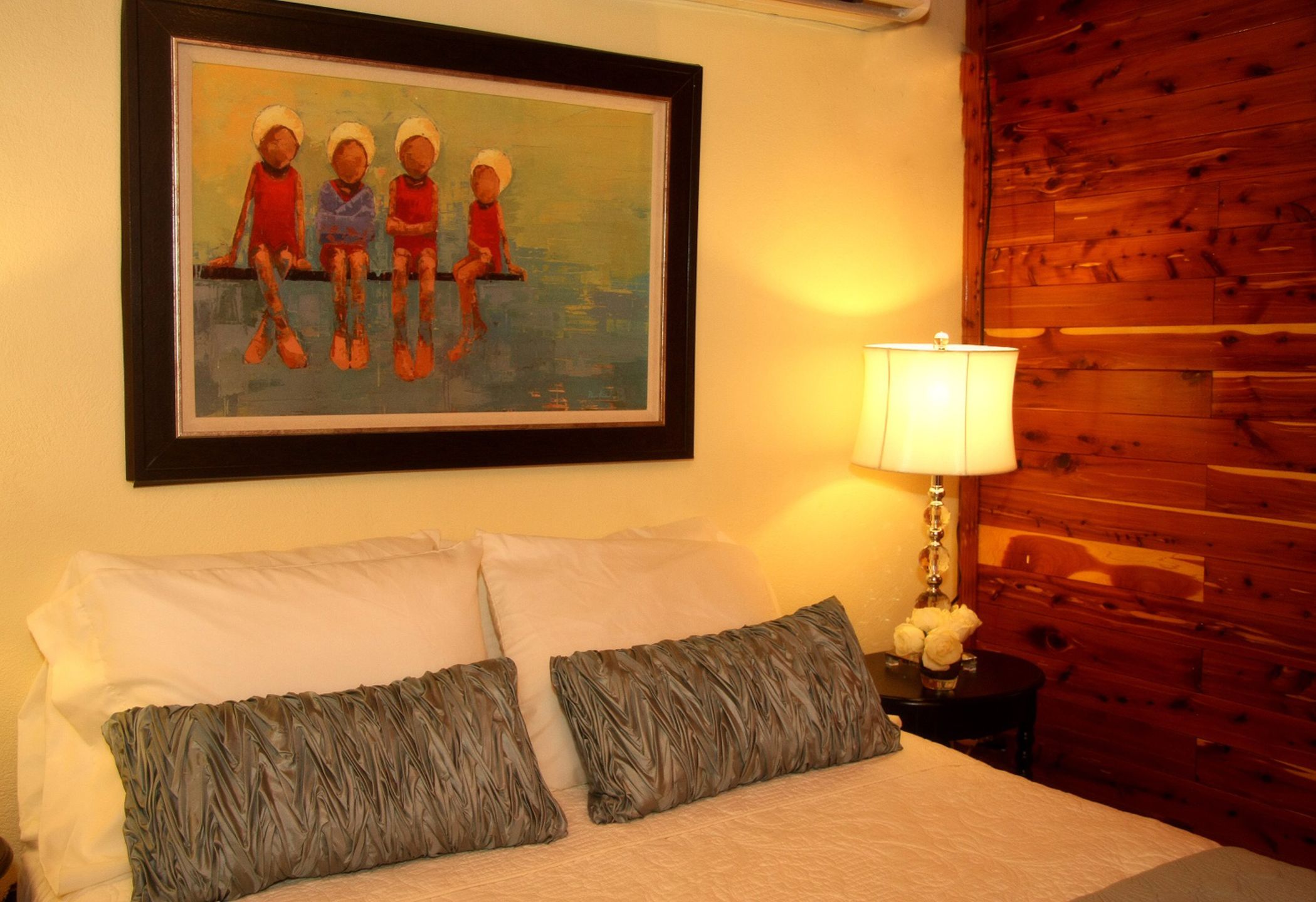 Una cama bien hecha con dos almohadas, un cuadro enmarcado encima y una pared de madera a la derecha.