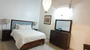 Un dormitorio con cama, mesitas de noche, cómoda, espejo y lámpara colgante.