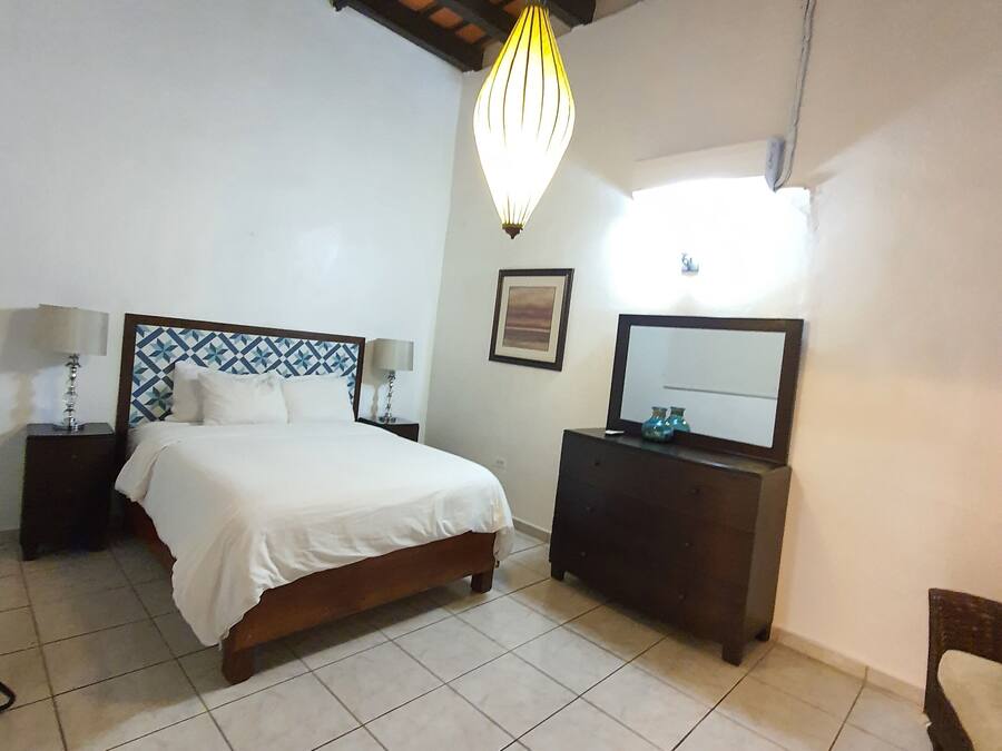 Un dormitorio con cama, mesitas de noche, cómoda, espejo y lámpara colgante.