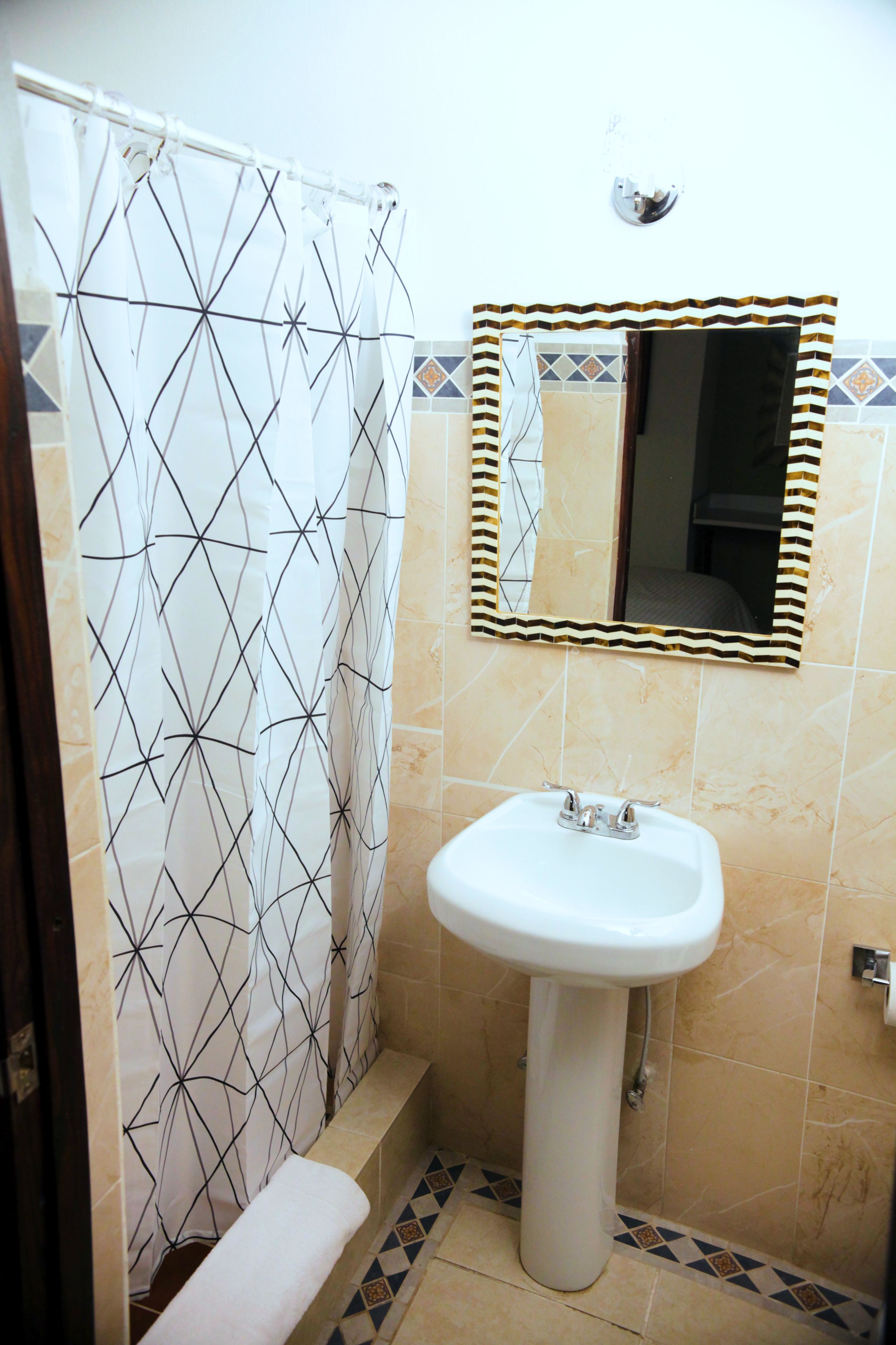 Un baño con cortina de ducha, lavamanos, espejo y paredes de azulejos.