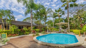 A wooden deck surrounding a swimming pool with palm trees and tropical plants. - Rarotonga Daydreamer Escape (Rarotonga)