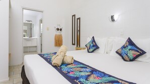 A hotel room with a bed, a nightstand, a mirror, and a door leading to a bathroom. - Rarotonga Daydreamer Escape (Rarotonga)