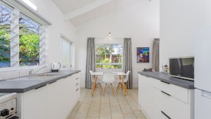 A modern kitchen with white cabinetry, a dining area with a table and chairs, and a view of the outdoors through large windows. - Rarotonga Daydreamer Escape (Rarotonga)