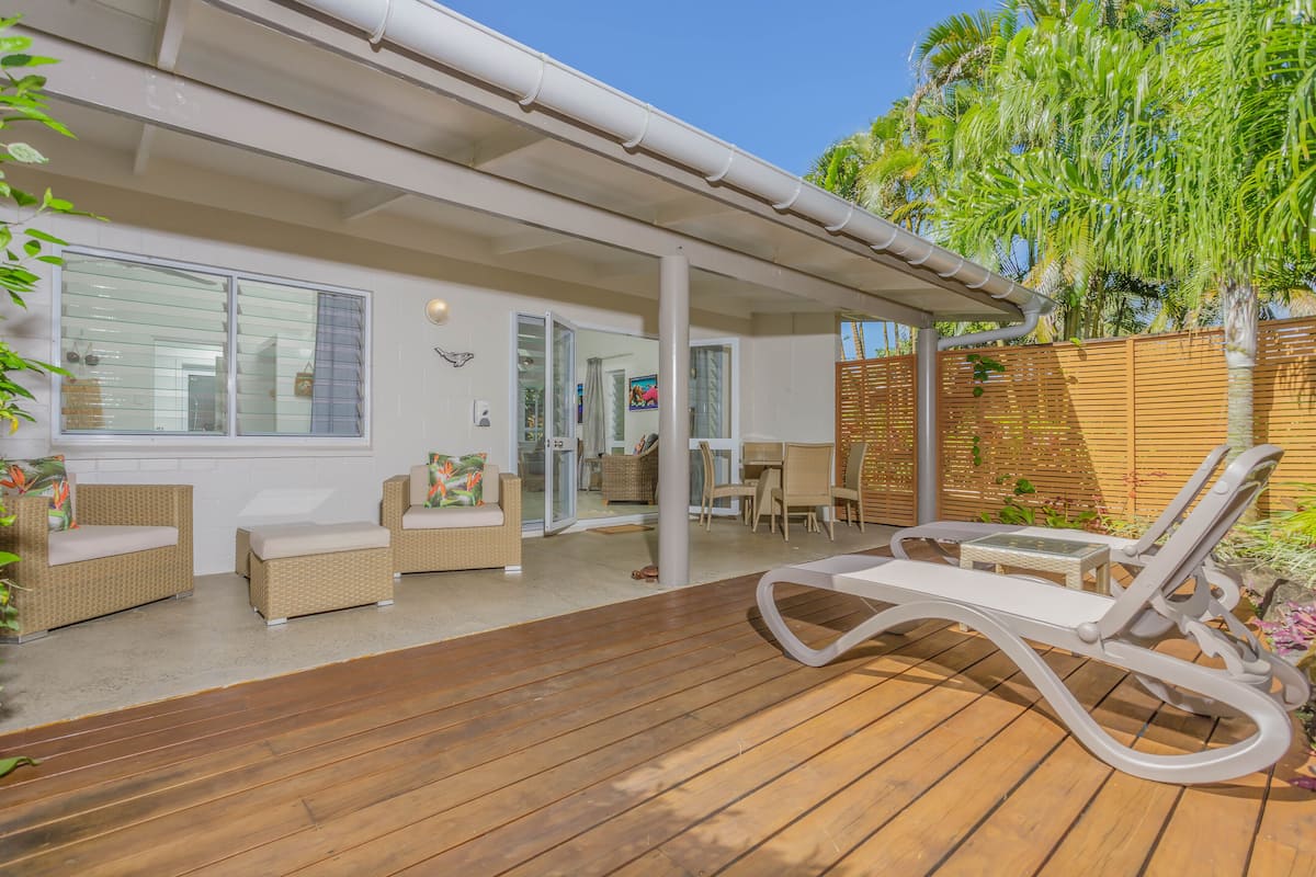 A covered patio with wicker furniture, a wooden deck, and a view of the interior.
