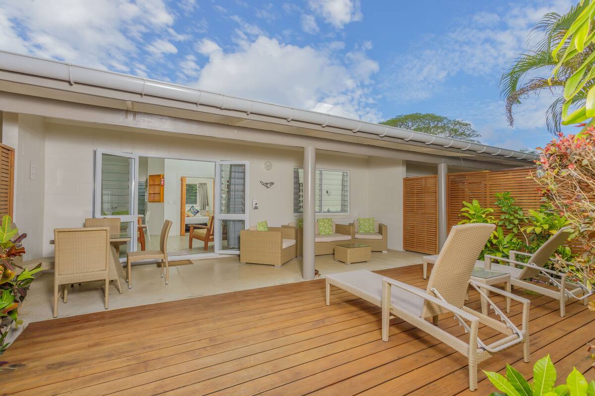 A covered outdoor area with a wooden deck, wicker furniture, and a glass door leading to an interior space.