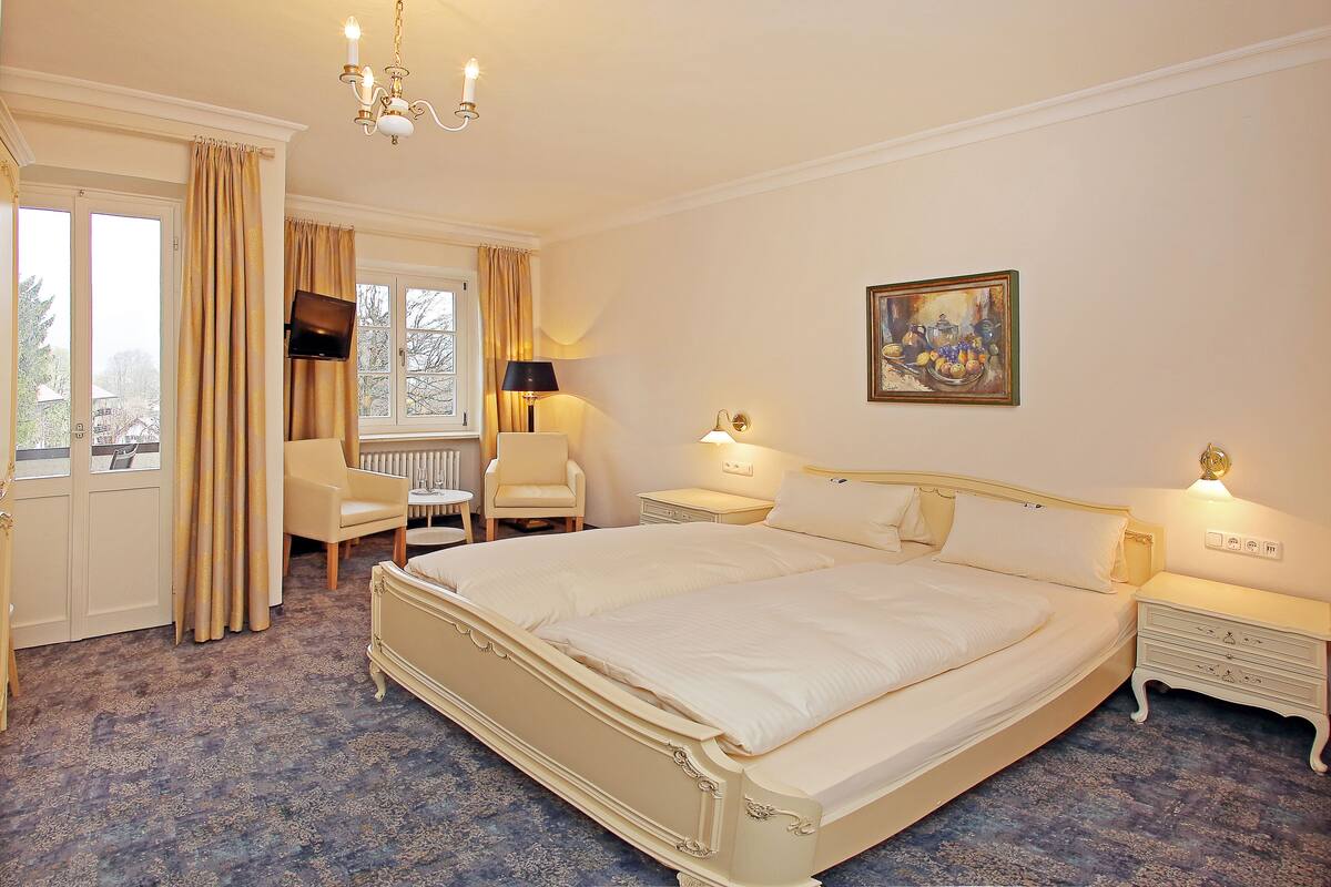 A spacious bedroom with a large bed, a bedside table, a chair, and a window with curtains.
