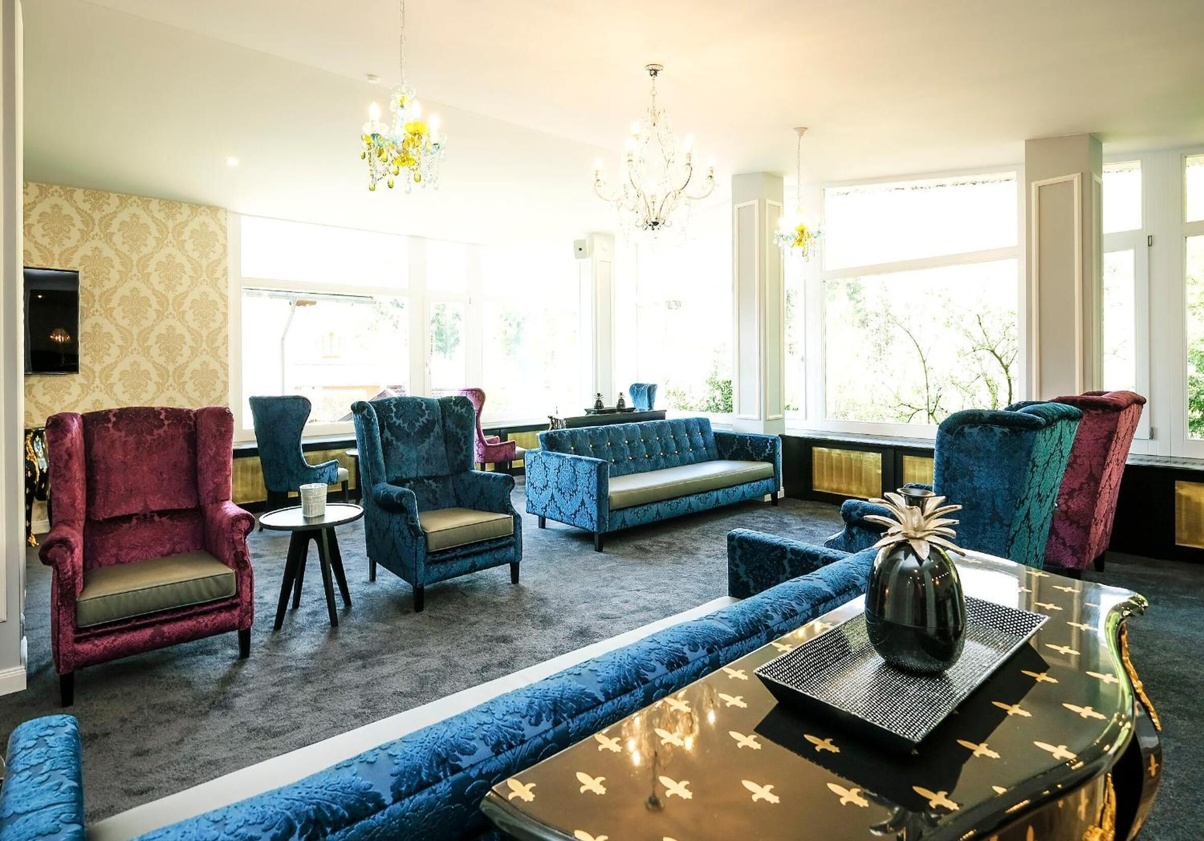 Un salón luminoso con un sofá azul, sillones rojos y una araña.