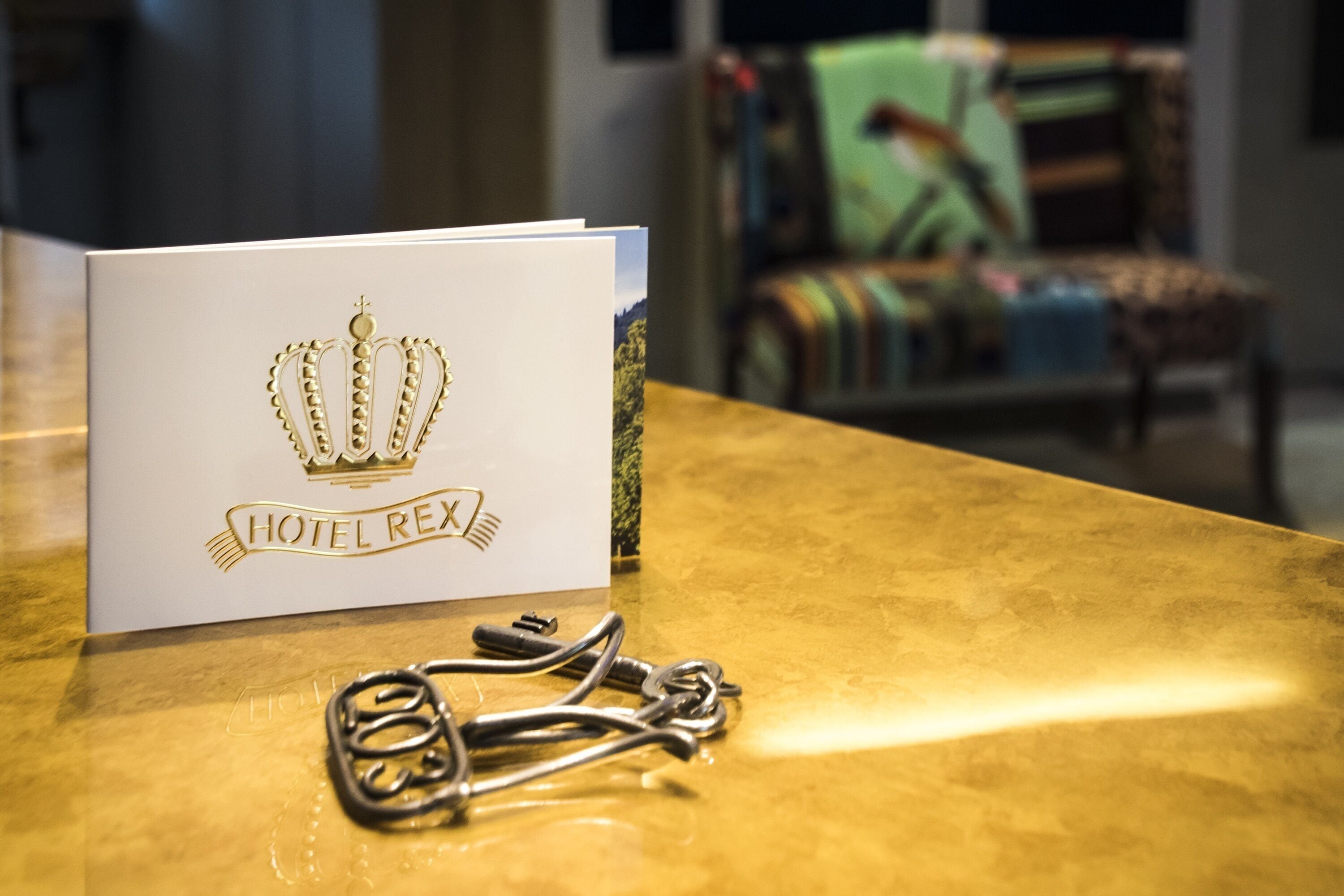 Una tarjeta blanca con una corona dorada y el texto "HOTEL REX" sobre una mesa dorada.