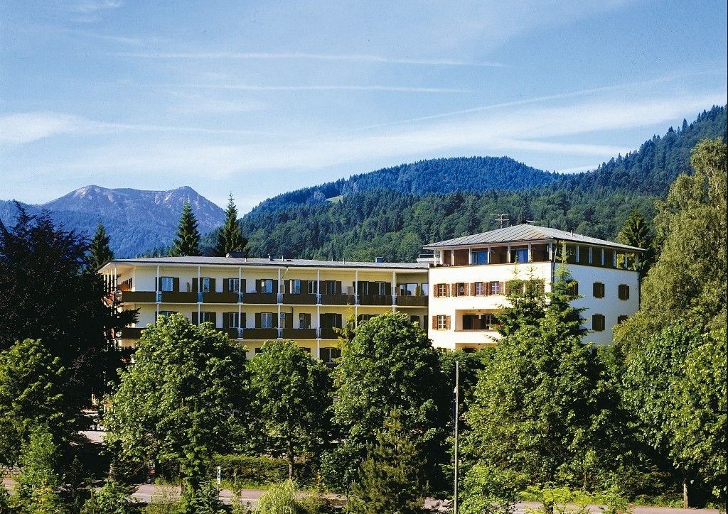 Un hotel de varios pisos con techo plano, rodeado de exuberante vegetación y montañas al fondo.