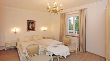 Un cuarto de hotel con una cama grande, dos mesitas de noche, un candelabro, una ventana con cortinas y un cuadro en la pared.