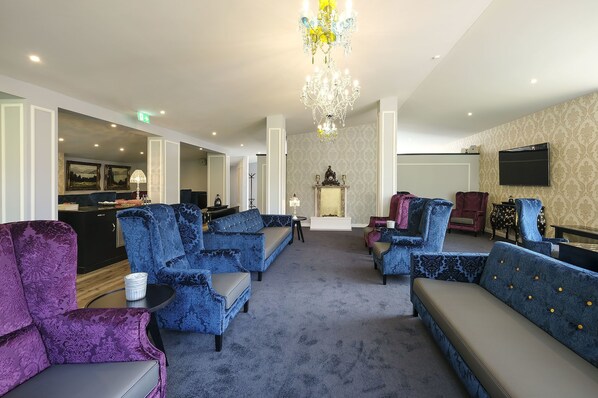 A spacious lobby with blue and purple upholstered seating, a chandelier, and a flat-screen TV on the wall.