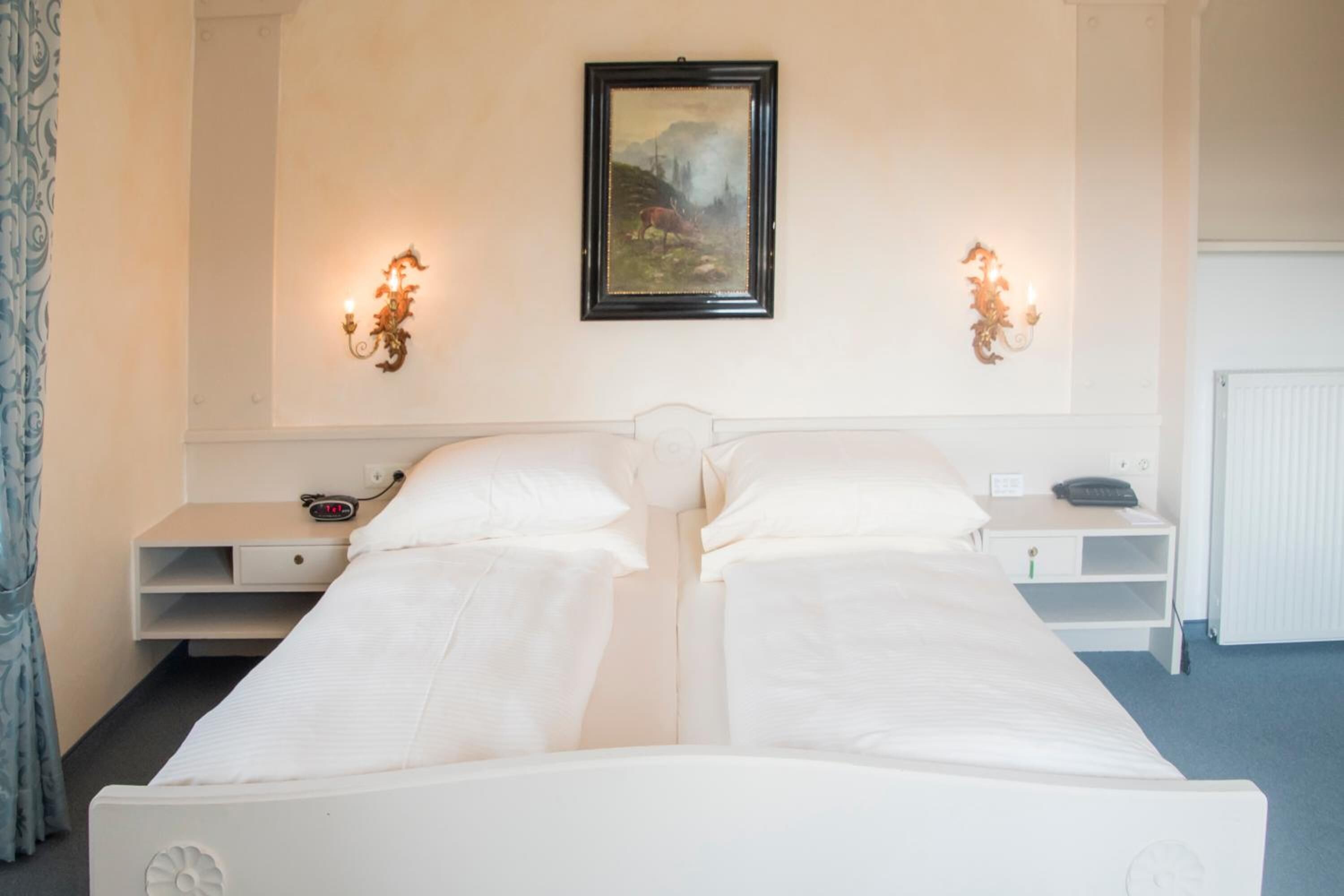 A twin room with a bed, bedside tables, a painting, and wall sconces.