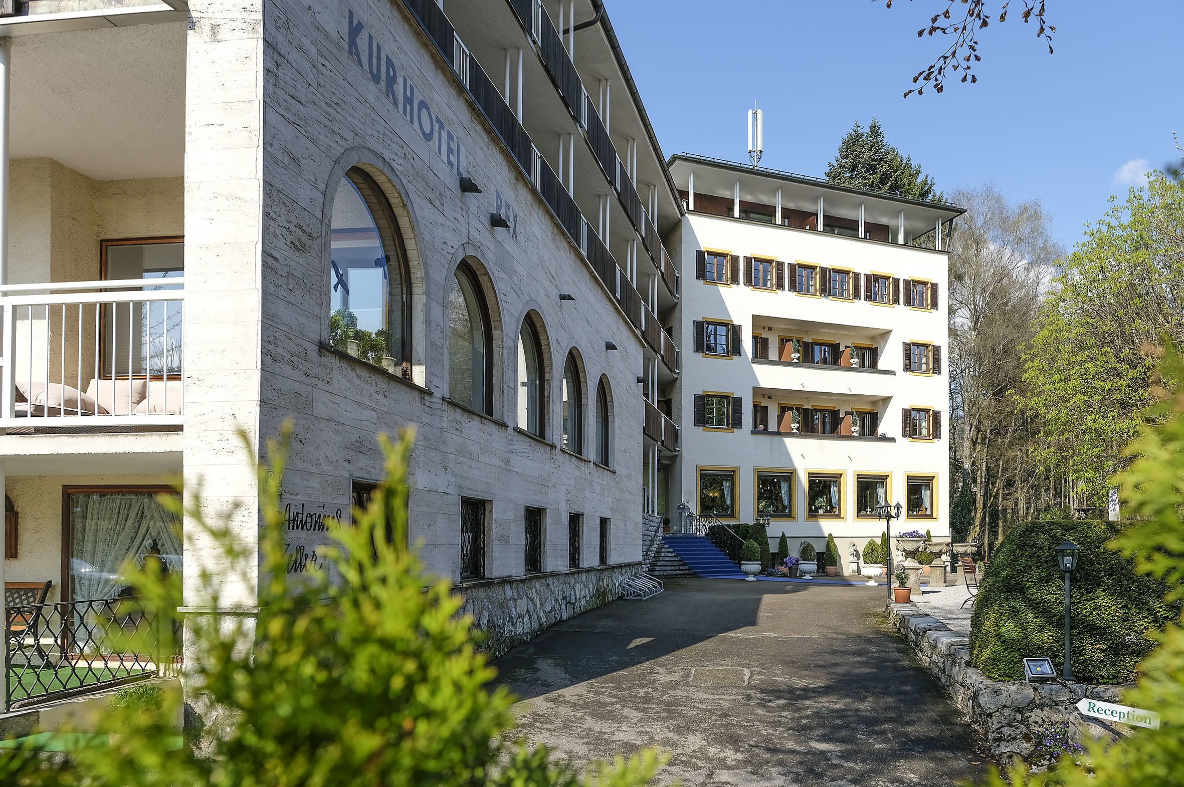 Un hotel con fachada blanca, varios balcones y un camino de piedra que conduce a la entrada.