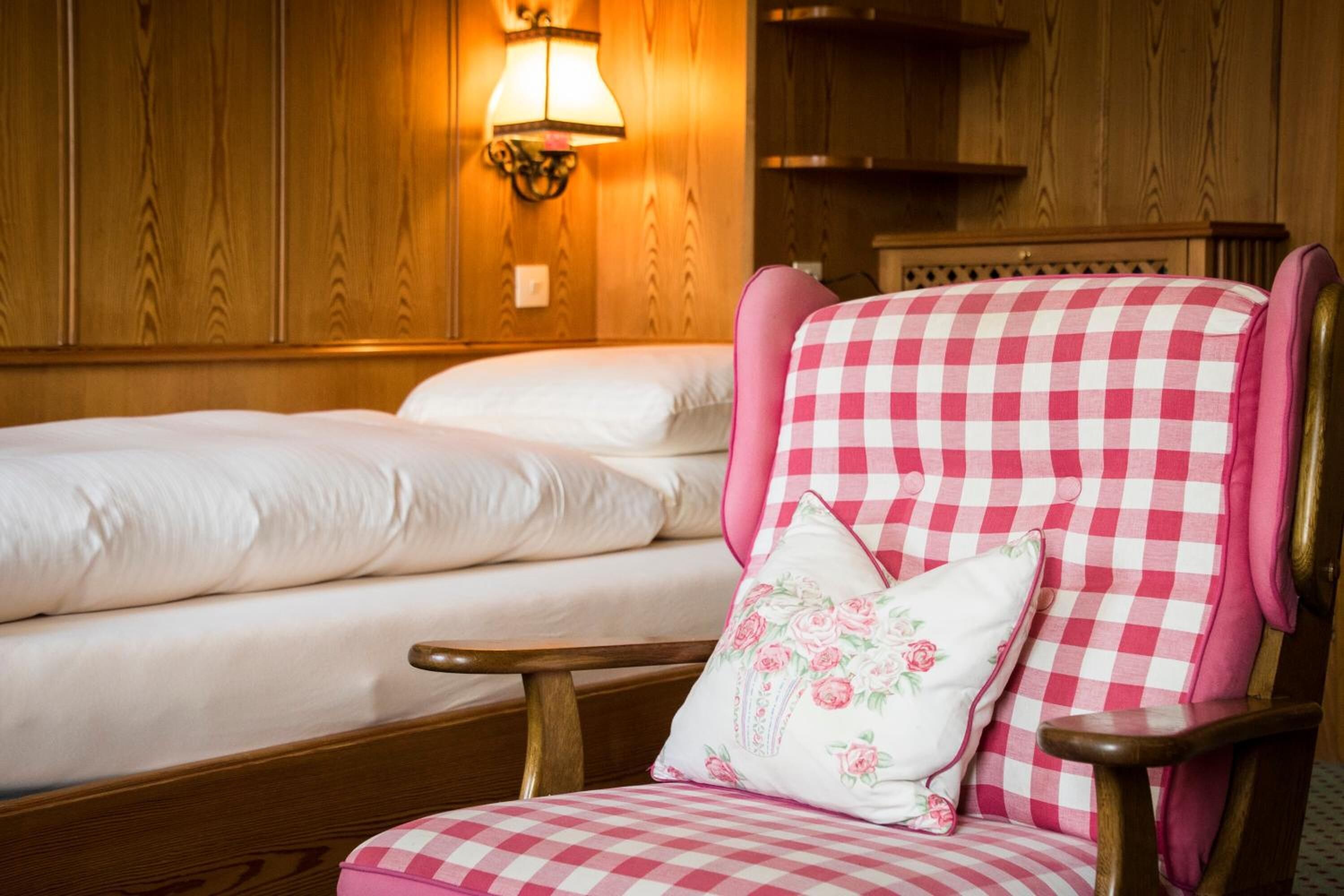 A hotel room with two beds, a checkered armchair, and a wall-mounted lamp.