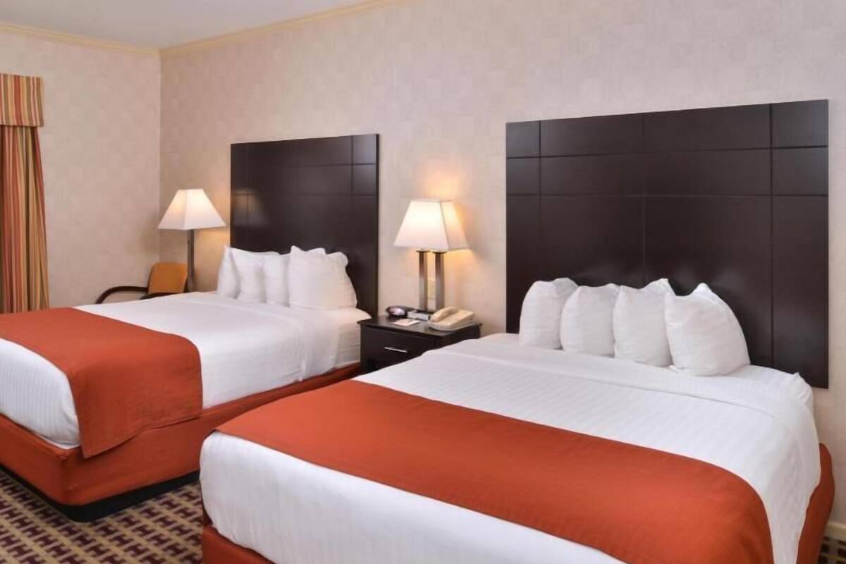 Habitación de hotel con dos camas, cada una con cabecero, mesitas de noche, lámparas y una alfombra estampada.