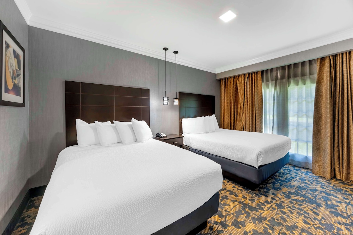 Habitación de hotel con dos camas, un cabecero grande, una mesita de noche y una ventana con cortinas.