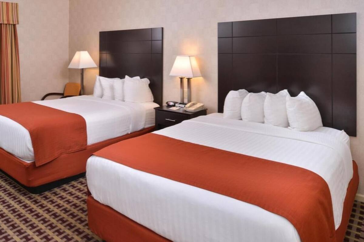 Habitación de hotel con dos camas, cada una con cabecero, mesitas de noche con lámparas y alfombra estampada.