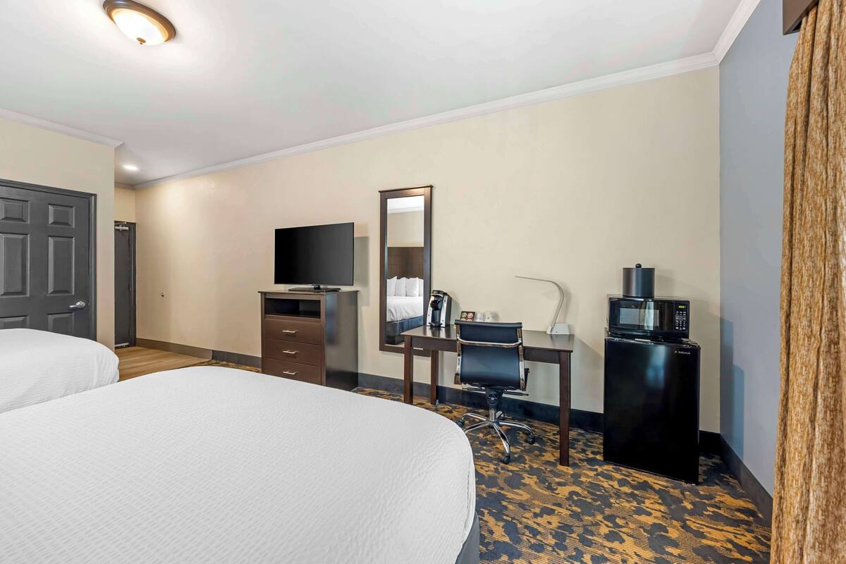 Habitación de hotel con dos camas, un escritorio con silla, televisor, microondas y espejo.