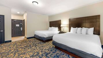 Quarto de hotel com duas camas, um tapete estampado, cabeceira escura e uma porta com uma placa.