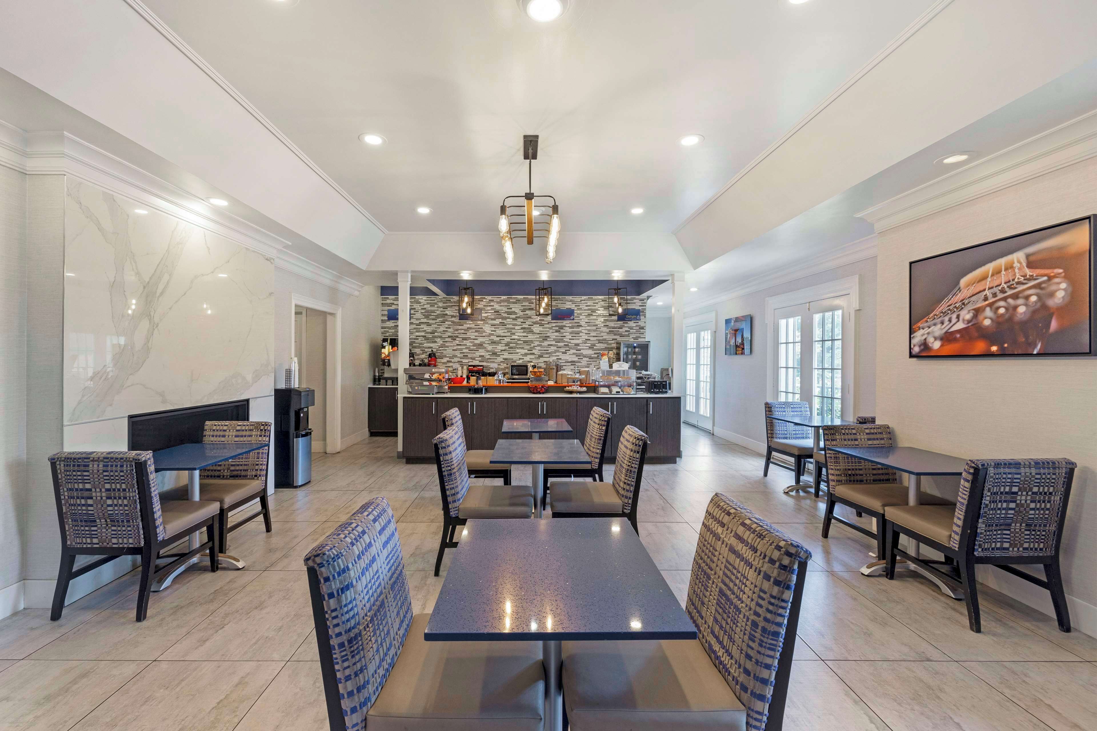 A spacious dining area with multiple tables and chairs, a central island with a kitchen, and a large window providing natural light.