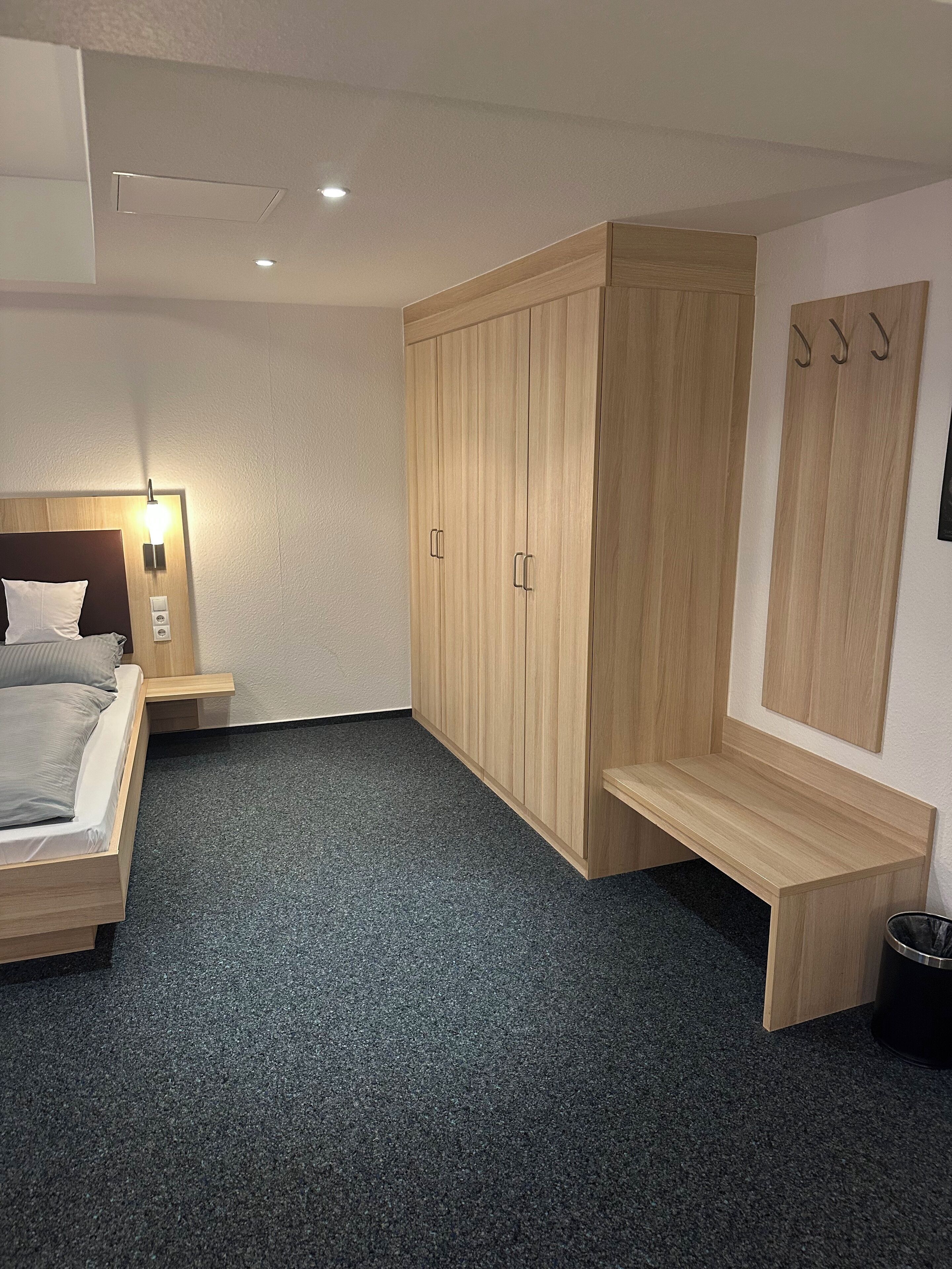 A bedroom with a bed, wooden wardrobe, bench, and hooks on the wall.