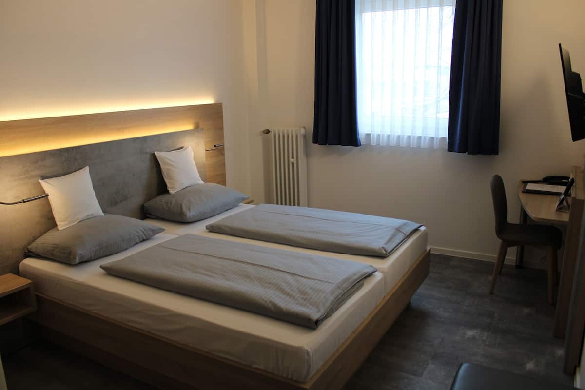 A hotel room with two beds, a desk, a chair, and a TV.