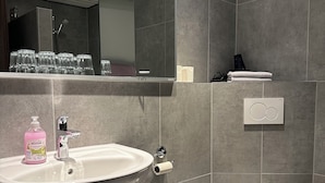 Um banheiro moderno com um espelho grande, pia com dosador de sabonete, vaso sanitário e porta-toalhas.