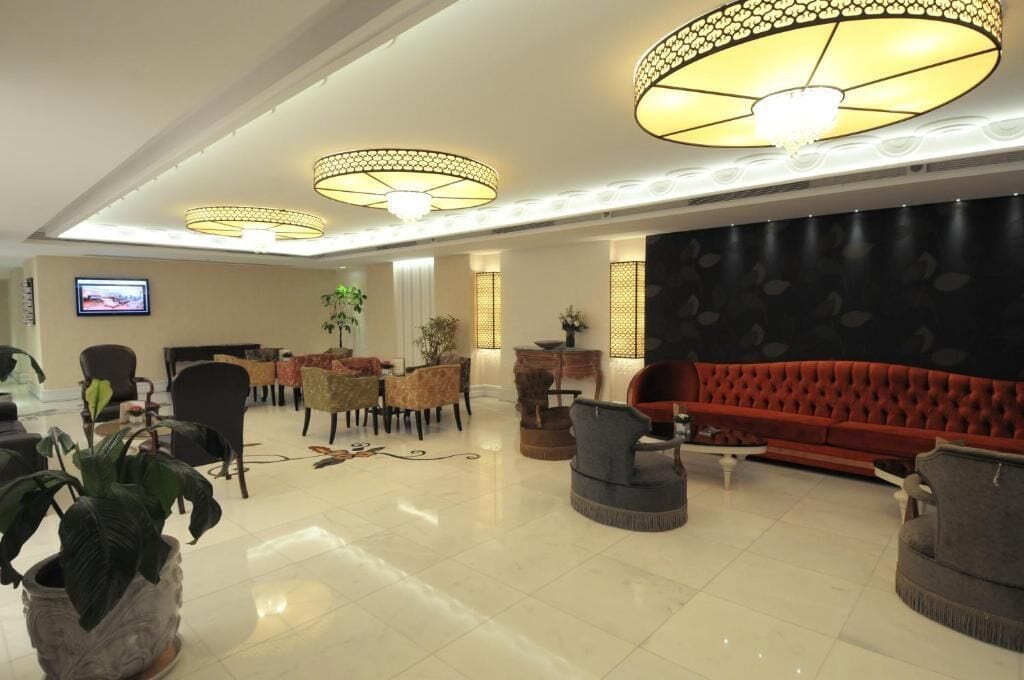 Un hall d’entrée spacieux, doté d’un canapé rouge, de plusieurs fauteuils, d’un téléviseur et d’éléments d’éclairage décoratifs.