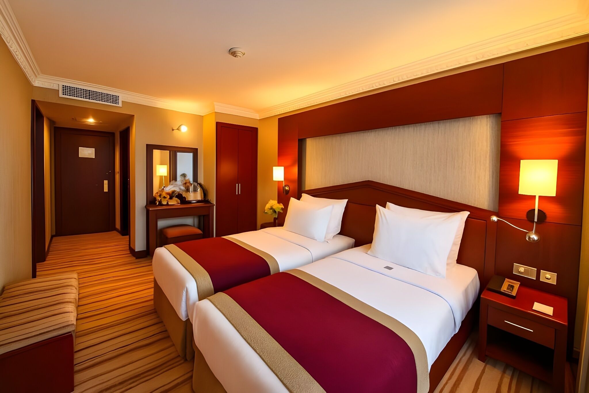 A hotel room with two beds, a desk, a chair, a nightstand, and a mirror.