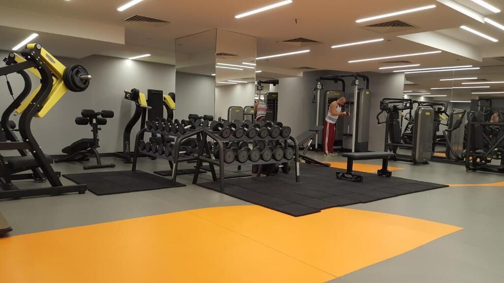 Uma academia com diversos equipamentos de exercício, incluindo halteres, aparelhos de musculação e um banco.