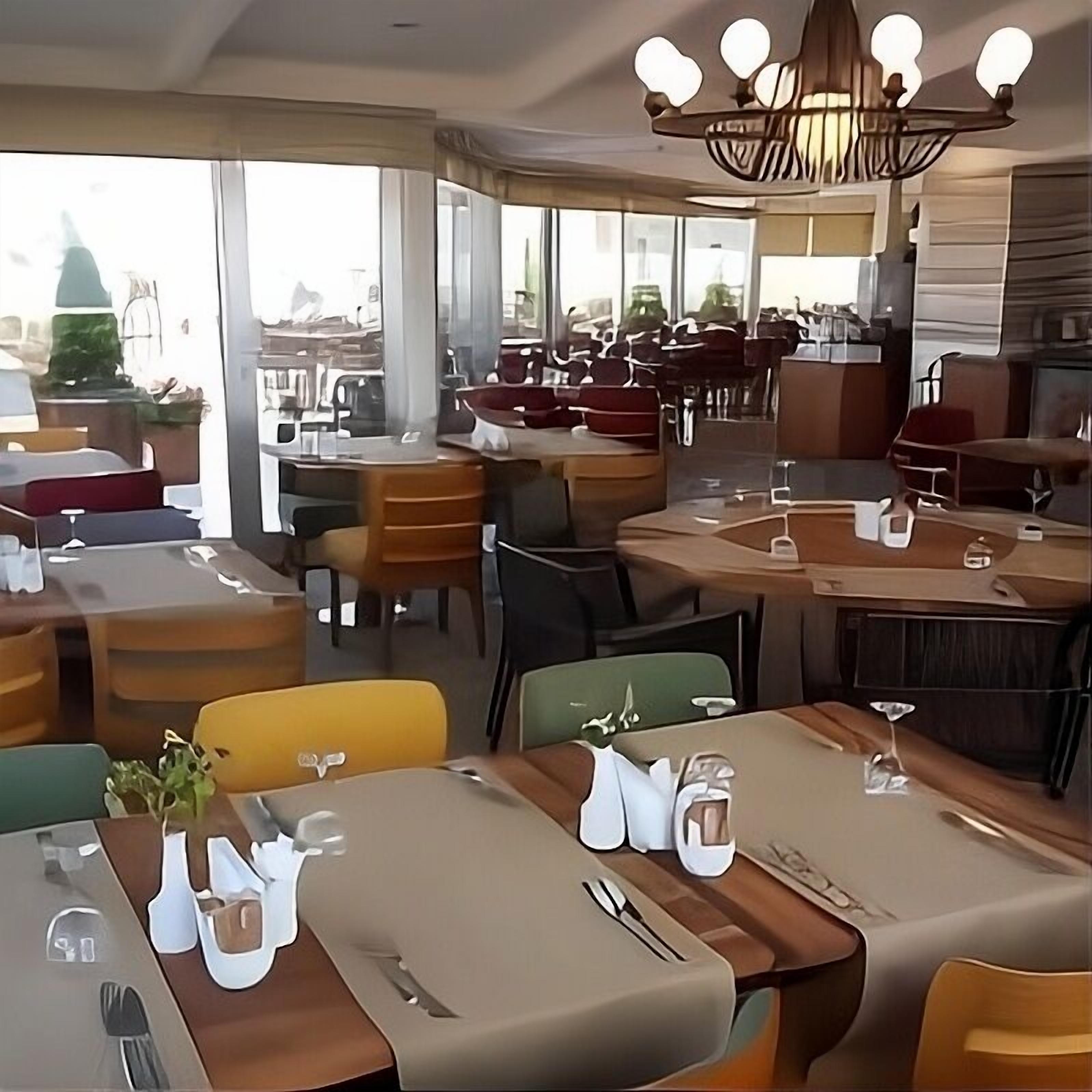 A restaurant with tables set for dining, a chandelier, and large windows.