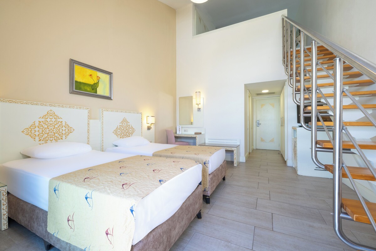 Habitación de hotel con dos camas, una escalera, un escritorio y un espejo.