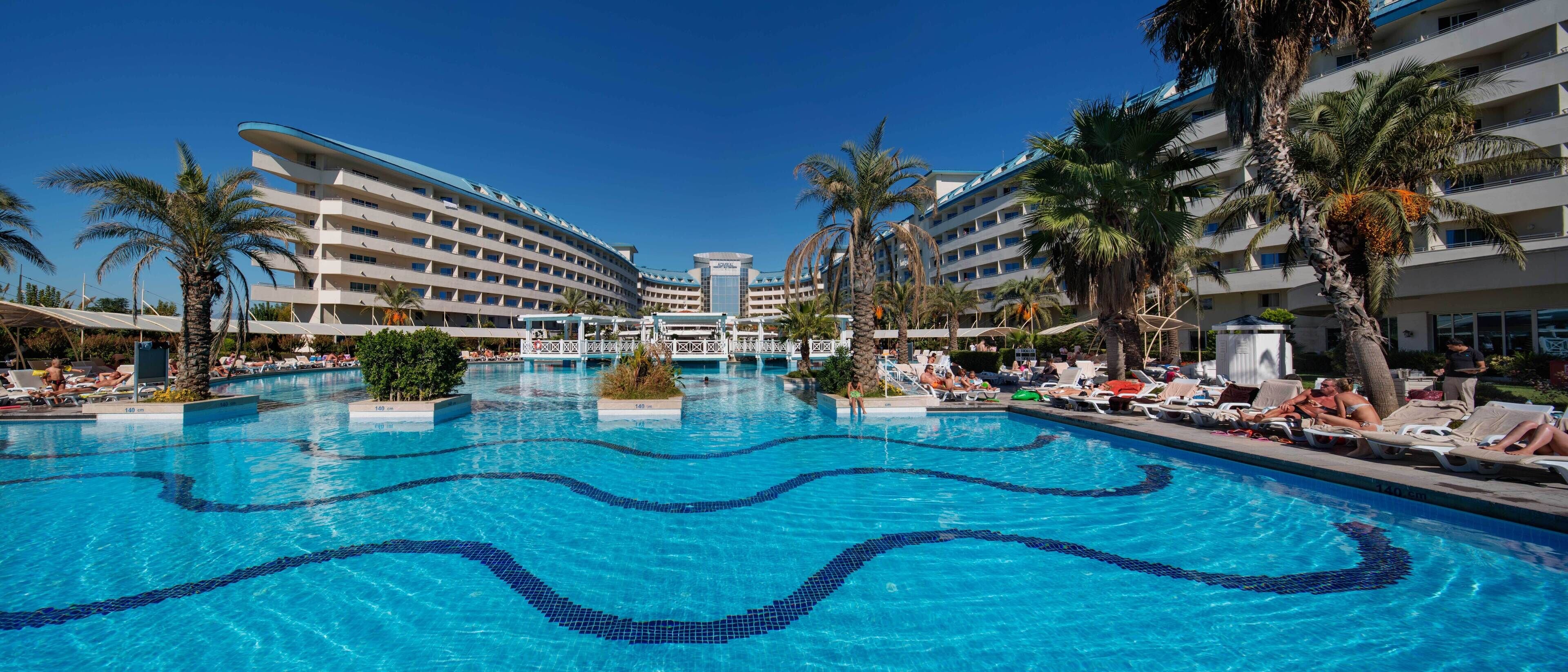 A hotel pool area with multiple levels of balconies, palm trees, and lounge chairs.